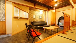 Una habitación japonesa tradicional con suelo de tatami, un sofá de cuero negro, una mesa de madera y una silla negra con cojines rojos.