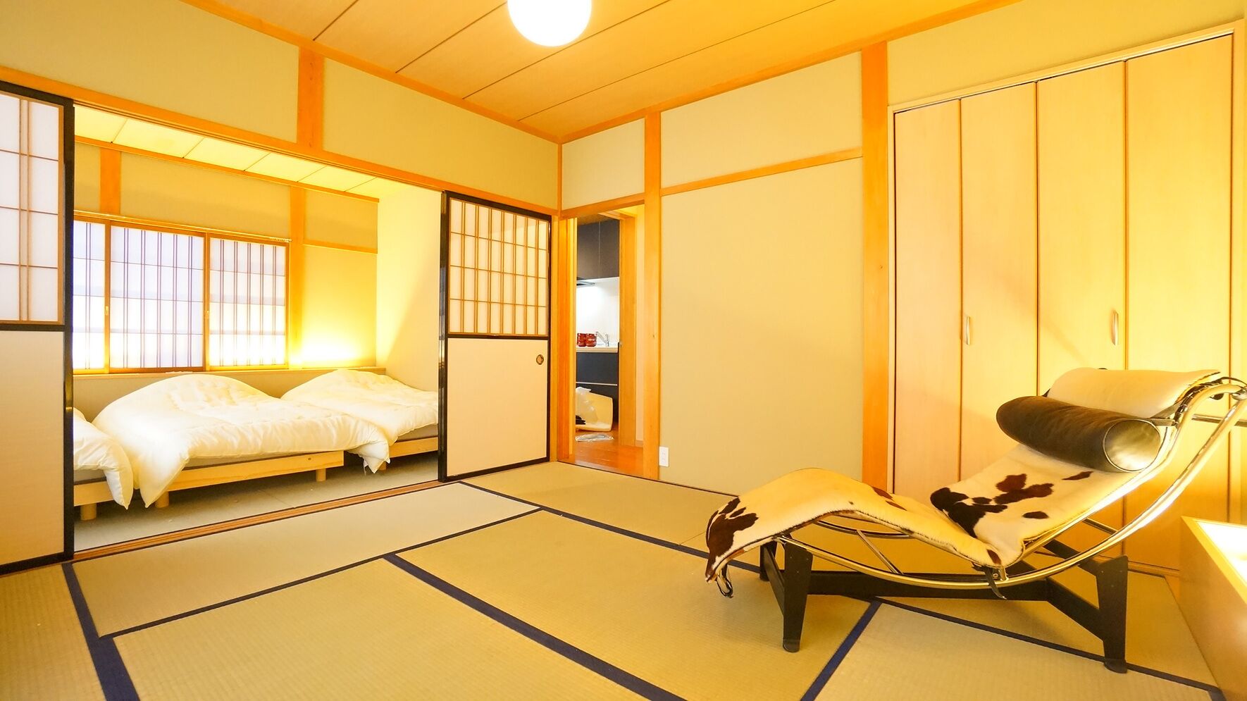Una habitación japonesa tradicional con suelo de tatami, un futón, una mesita baja y una silla con funda de cuero de vaca.