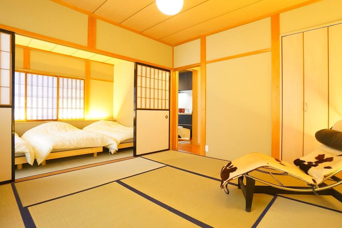 A traditional Japanese room with tatami flooring, a futon bed, a low table, and a chair with a cowhide cover.