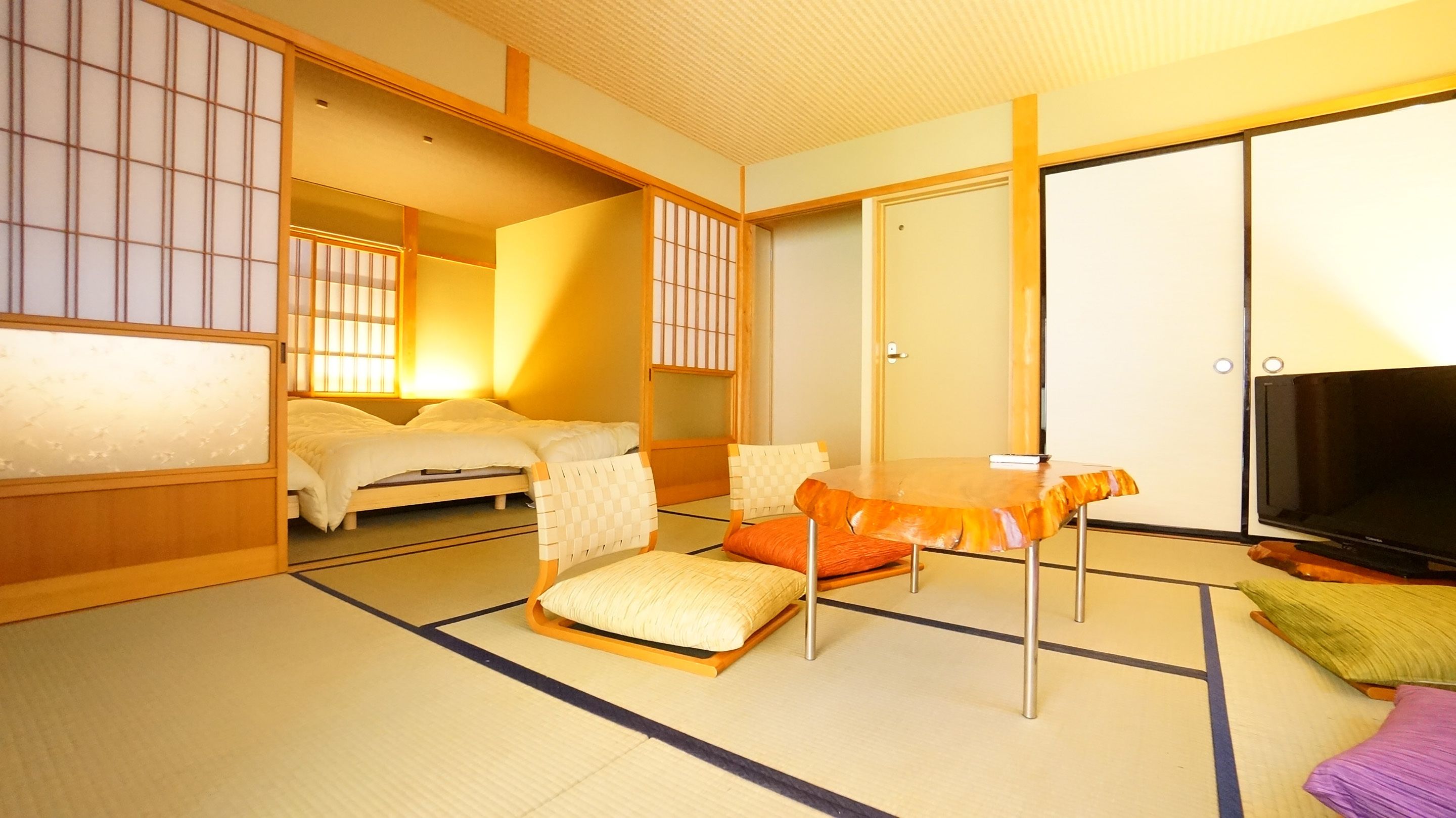 Une pièce de style japonais traditionnel, avec un sol recouvert de tatamis, un lit, une table avec des coussins et un téléviseur.