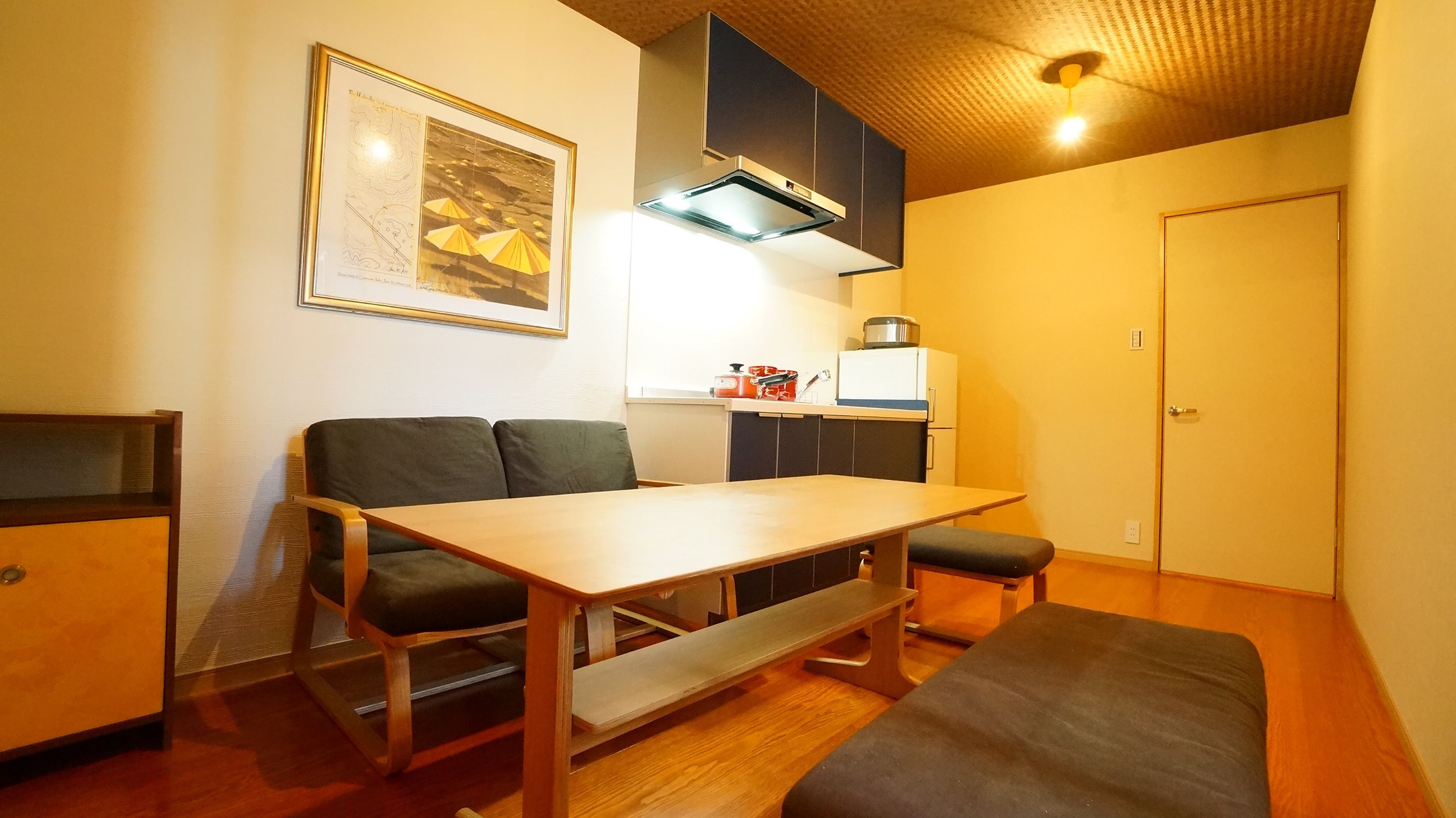 Un espacio habitable compacto con kitchenette, una mesa de comedor, un sofá y un banco.
