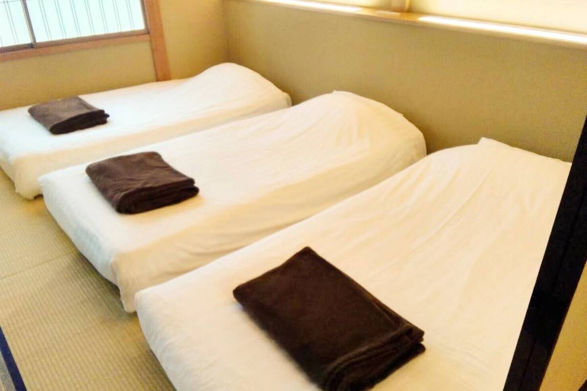 Three single beds with white linens and brown towels, arranged in a row.