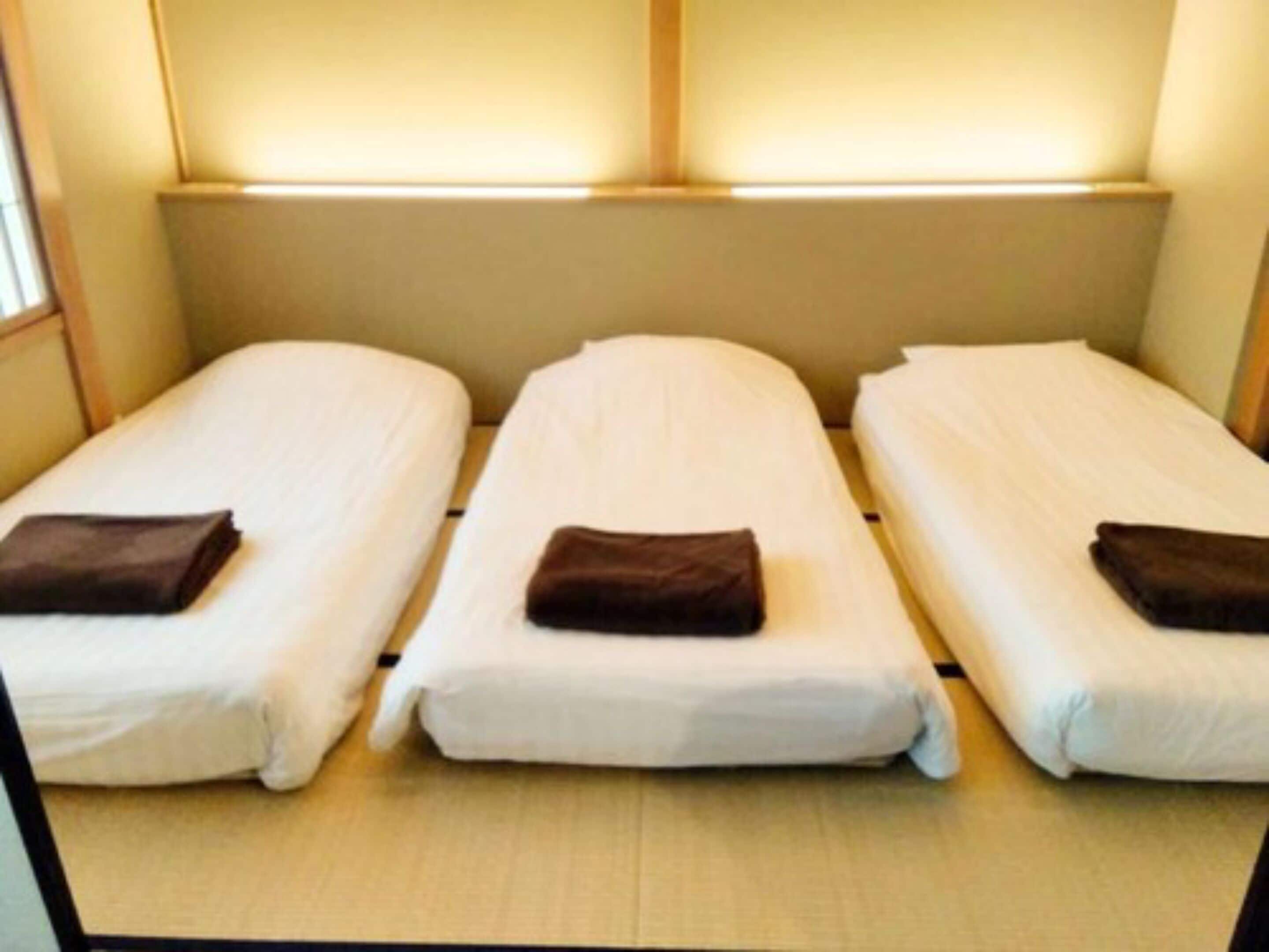 Una habitación con tres camas individuales dispuestas una al lado de la otra, cada una con una almohada y un edredón doblado.