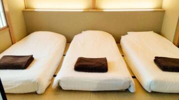 Una habitación con tres camas individuales dispuestas una al lado de la otra, cada una con una almohada y un edredón doblado.