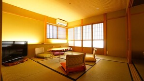 Una habitación japonesa tradicional con suelo de tatami, una mesa baja, cojines y un televisor.