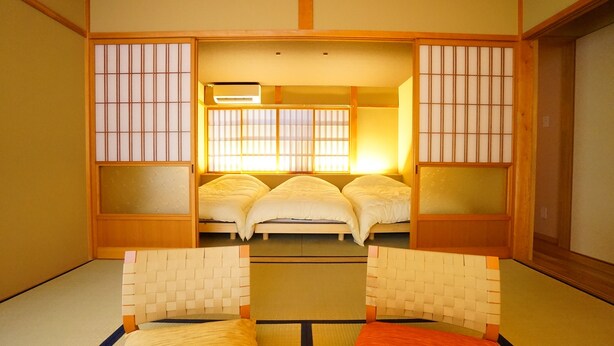 Una habitación japonesa tradicional con suelo de tatami, futón, puertas correderas y un separador shoji.