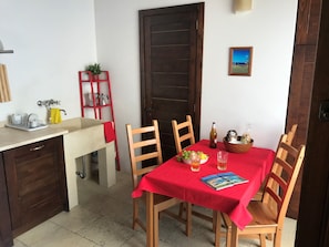 A dining area with a red tablecloth, wooden chairs, a bowl of fruit, a bottle, and a glass of beer.