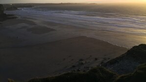 Un paysage côtier avec une plage, des vagues et un coucher de soleil.