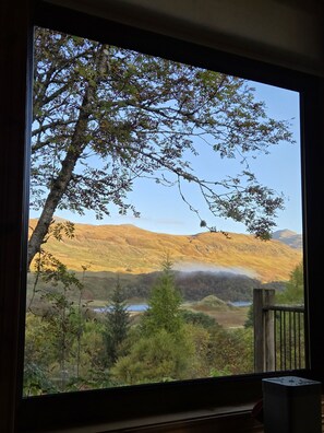 Blick aus einem Fenster auf eine gebirgige Landschaft mit einem See und bewaldetem Gebiet.
