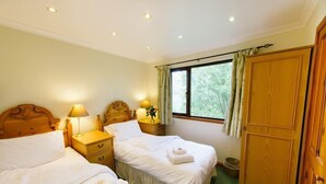 A hotel room with two beds, wooden headboards, bedside tables with lamps, a large wardrobe, and a window with curtains.