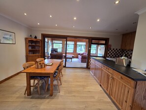 A spacious kitchen with wooden cabinets, a dining table with chairs, and a view through the glass door to an outdoor seating area.