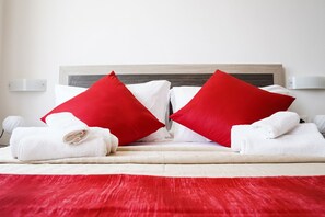 A neatly made bed with white and red pillows, white towels, and a red bedspread. - Hotel Virgilio (Taranto)