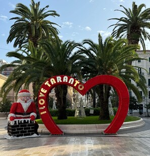 A heart-shaped sign with "I ♥ TARANTO" written on it, a Santa Claus figure, and palm trees in the background. - Hotel Virgilio (Taranto)