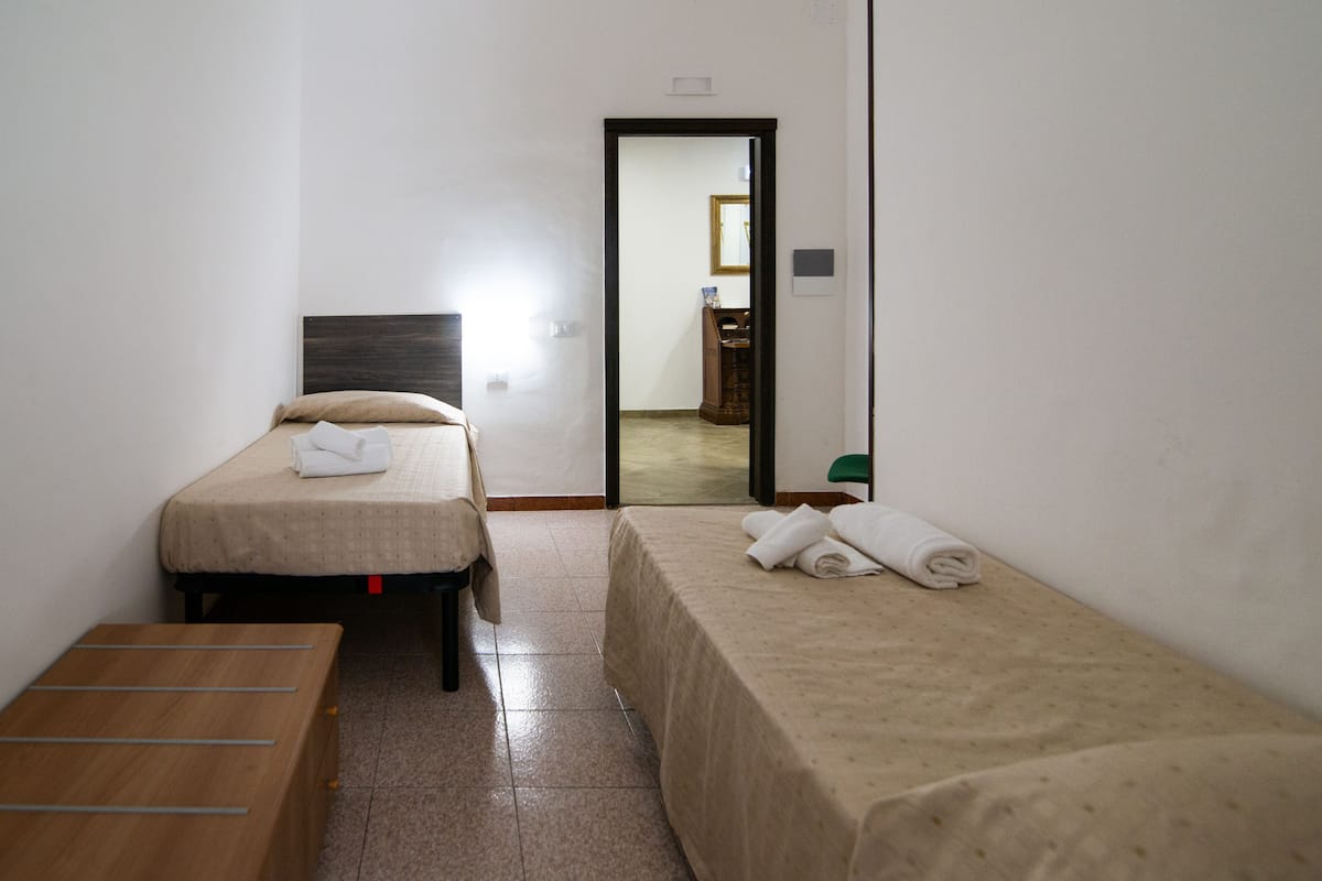 A small, clean room with two beds, a wooden bench, and a mirror.