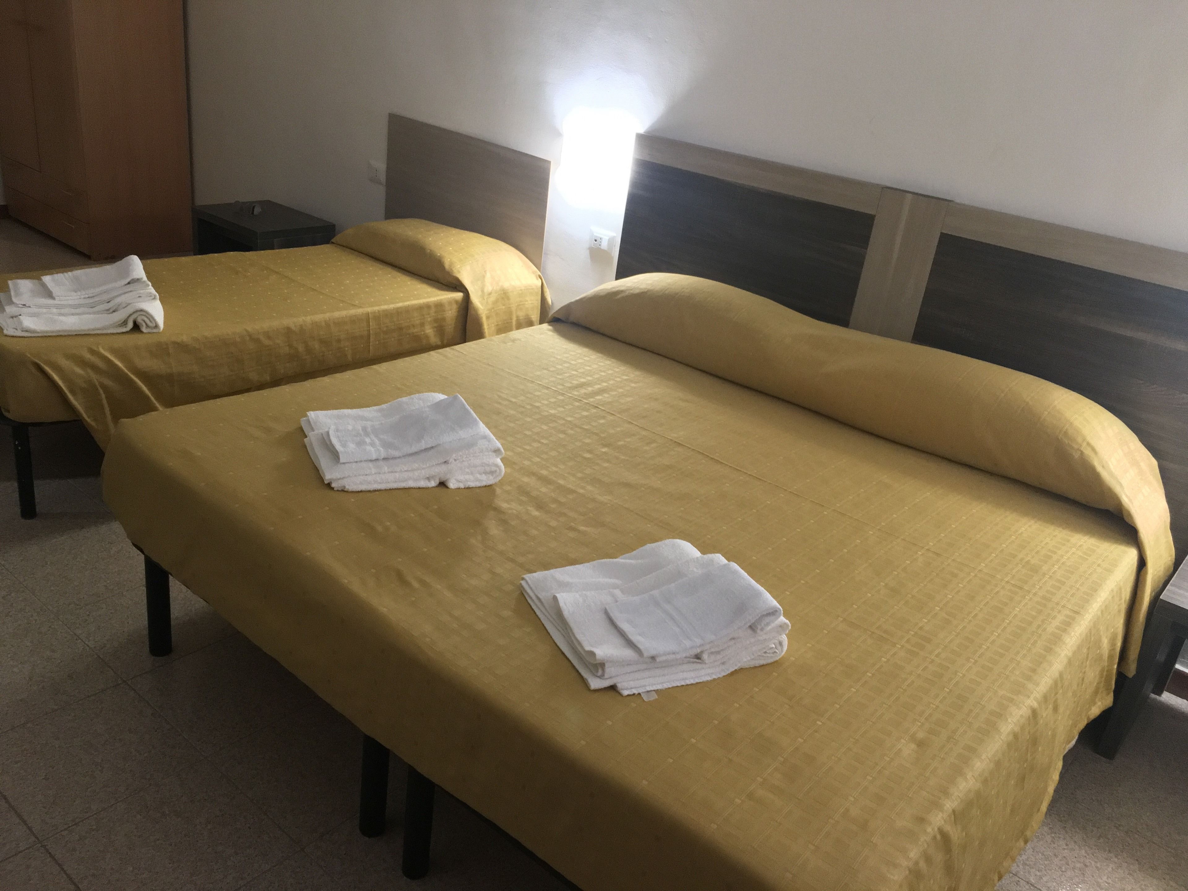 Dos camas individuales con ropa de cama amarilla y toallas blancas, un cabecero de madera y una mesita de noche con lámpara.