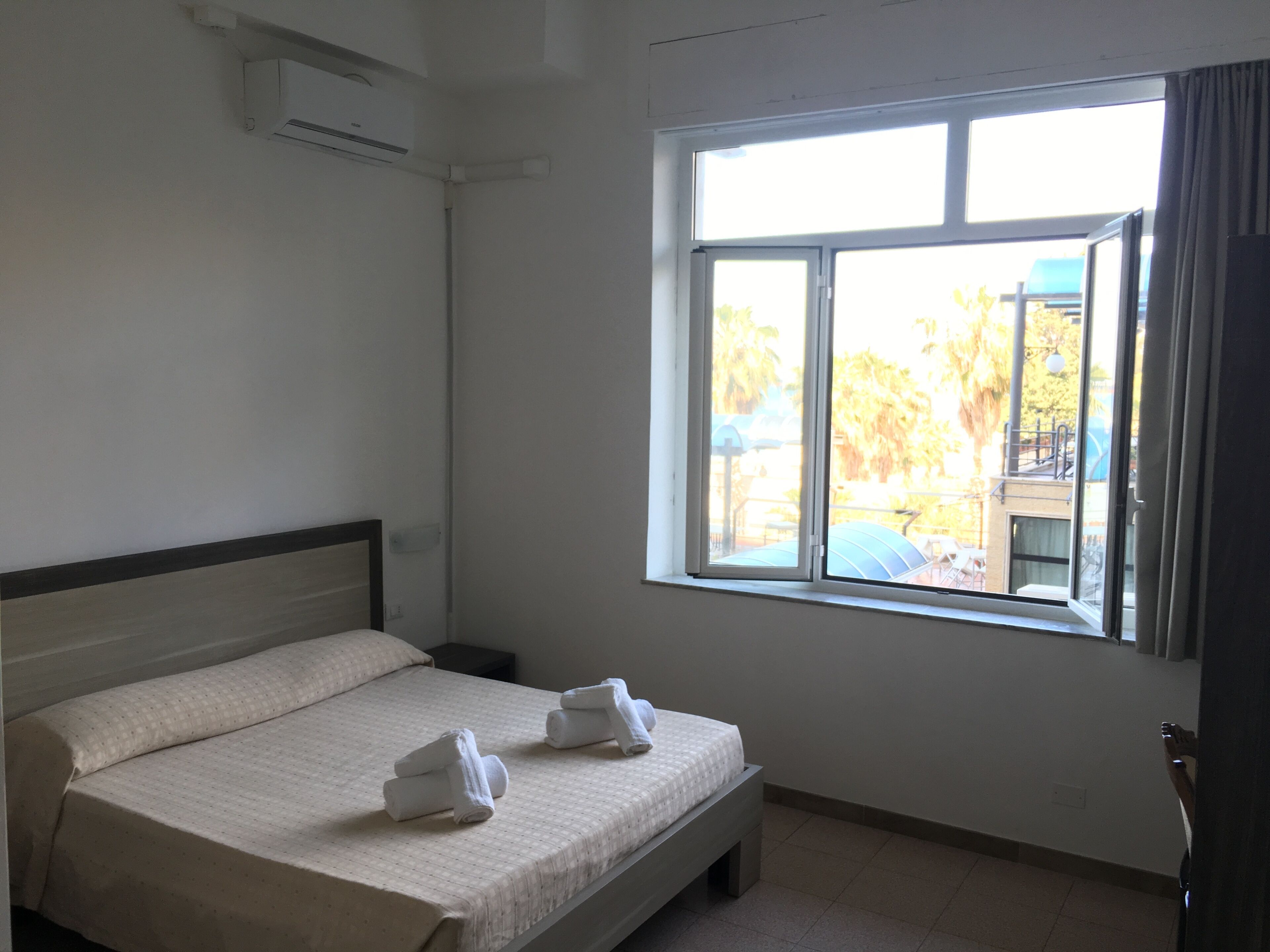 A hotel room with a bed, a window, and an air conditioning unit.