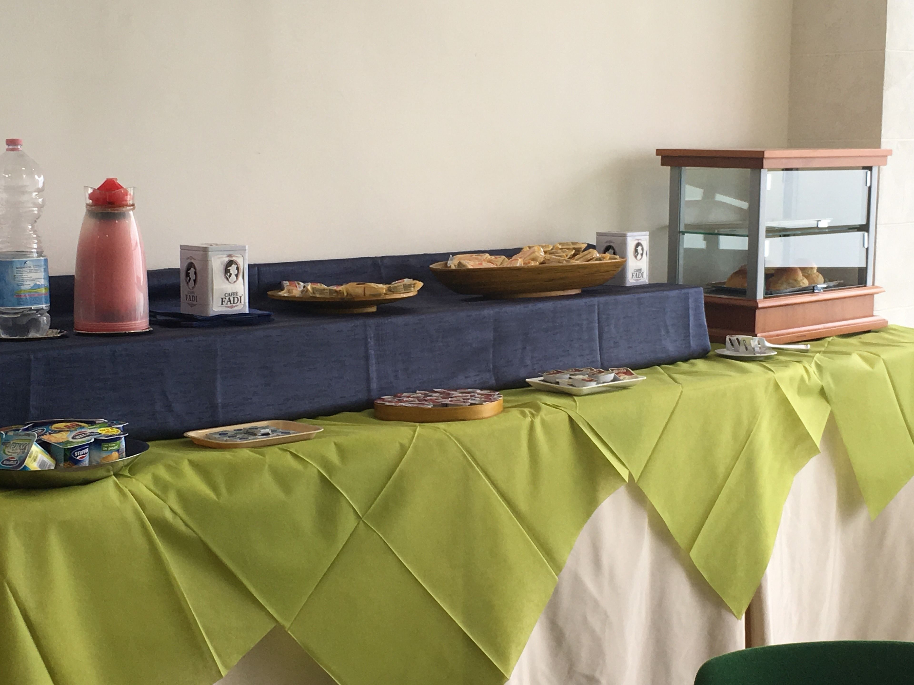 Una mesa con un mantel verde, donde se ha dispuesto un bufé variado de alimentos y un dispensador de agua.