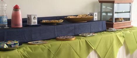 Una mesa con un mantel verde, donde se ha dispuesto un bufé variado de alimentos y un dispensador de agua.