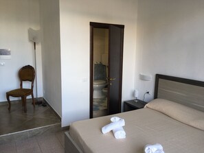 A hotel room with a bed, a chair, a bedside table, a nightstand, and a bathroom visible through an open door. - Hotel Virgilio (Taranto)