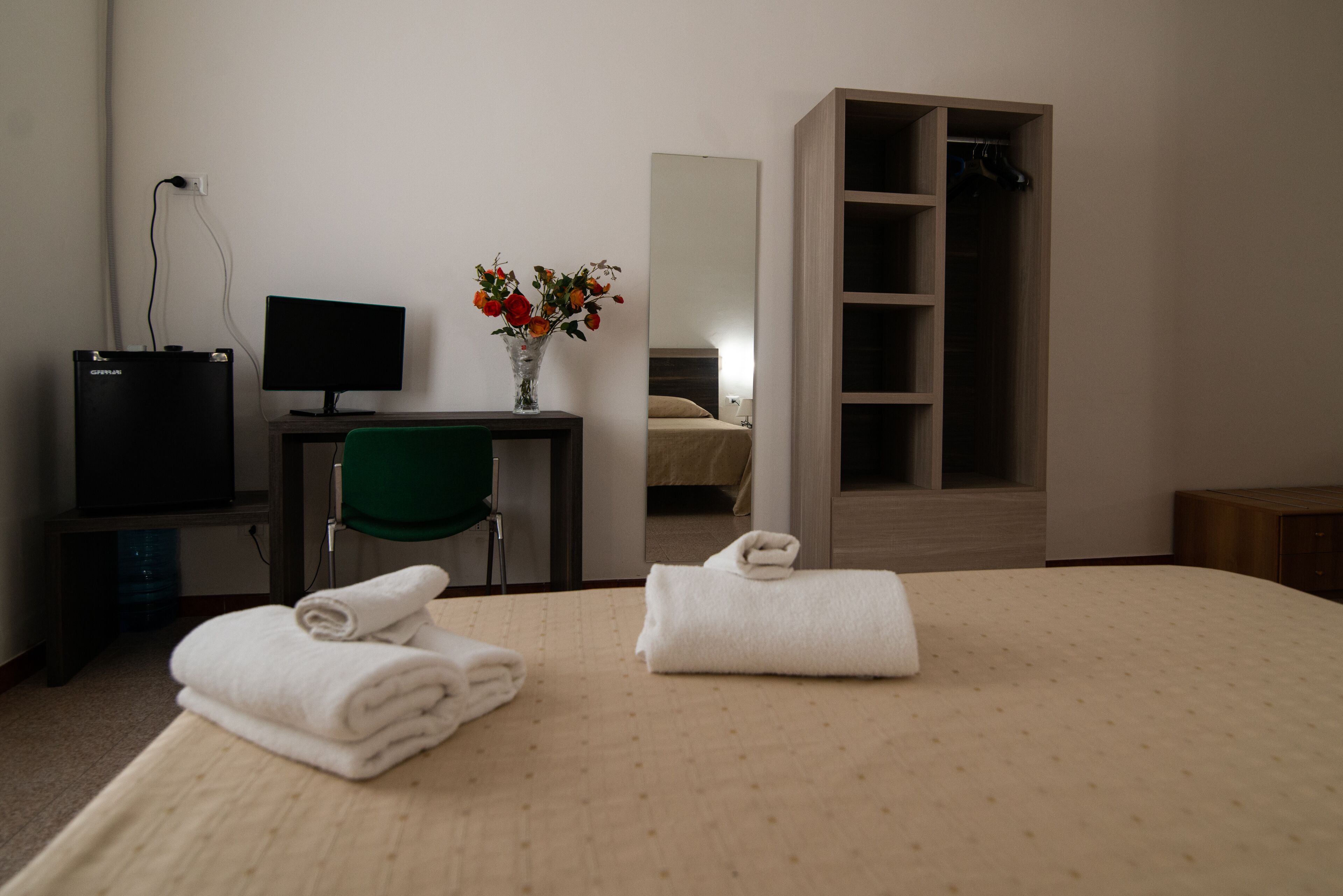 Una camera d'albergo con un letto, una scrivania con un computer, una sedia, uno specchio e un armadio.