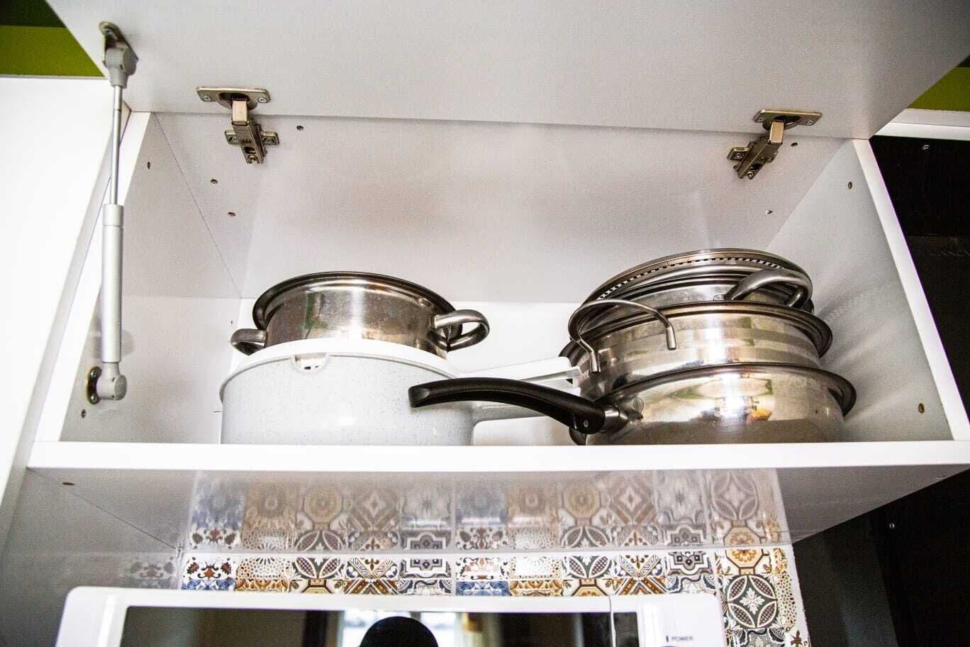 Un armario de cocina con dos ollas de acero inoxidable y una olla blanca.