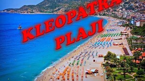 Ein Strand mit vielen Sonnenschirmen und Menschen, beschriftet 'KLEOPATRA PLAJI'.