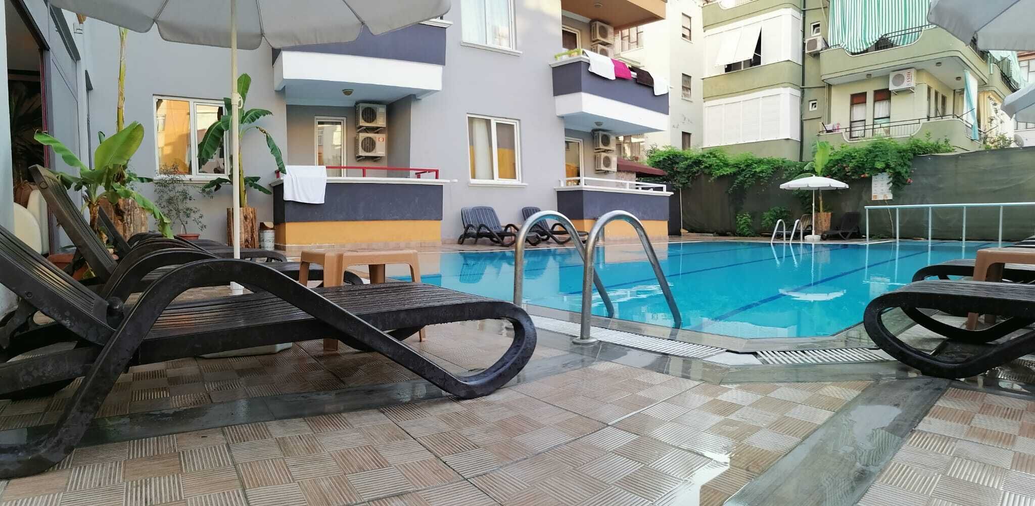 Una piscina interior con sillones de descanso, suelo de baldosas y un edificio con balcones al fondo.