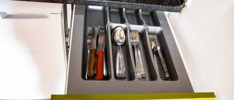A kitchen drawer with utensils and a yellow handle.