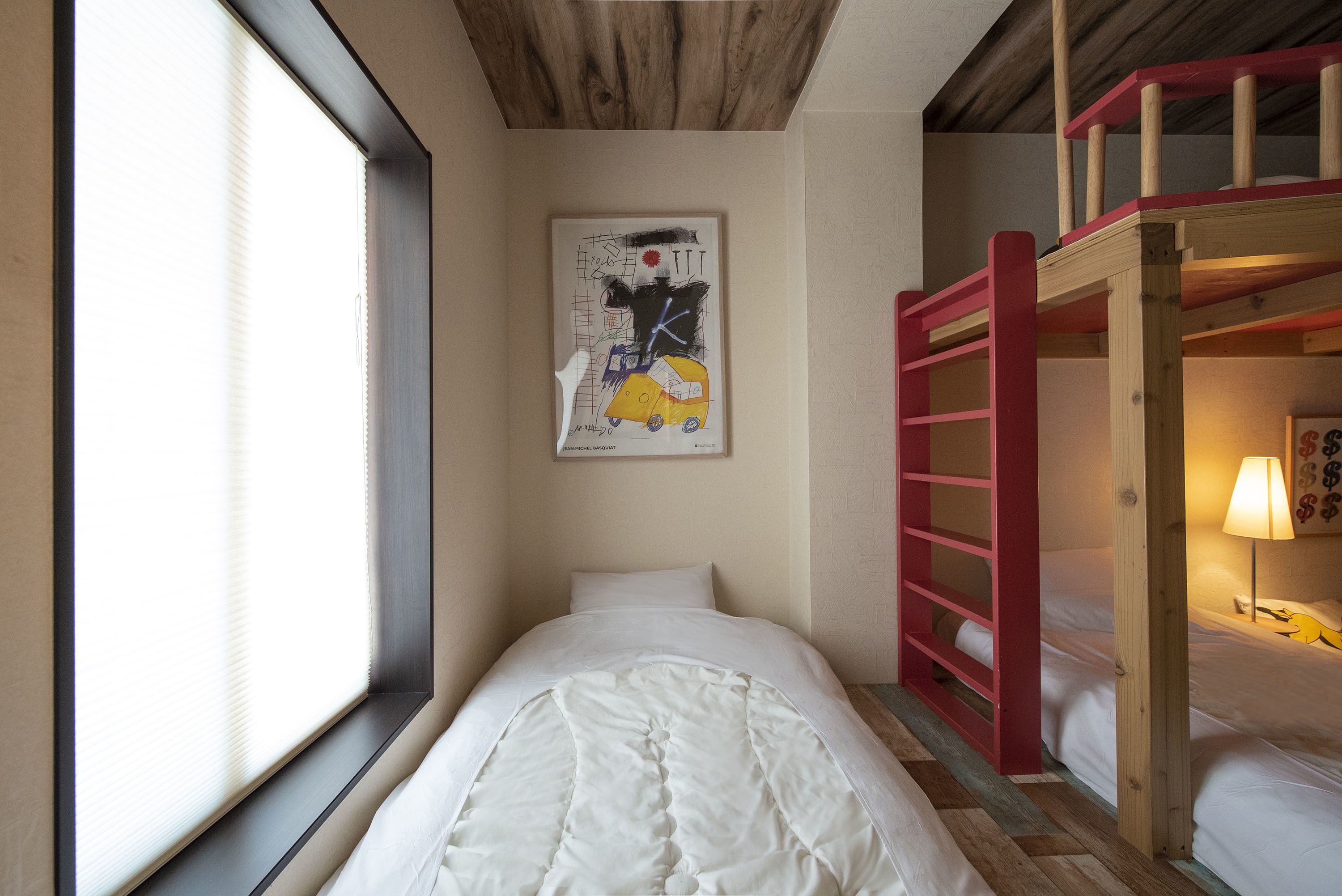 Ein Schlafzimmer mit einem Etagenbett, einem Bett mit weißer Bettdecke, einem Fenster mit Jalousien und einem Wandbild.
