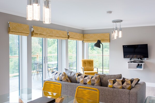 Una sala de estar moderna con sofá, sillas amarillas, televisor y ventanas grandes.