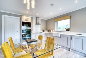 A modern kitchen with white cabinets, a glass dining table, and yellow chairs.
