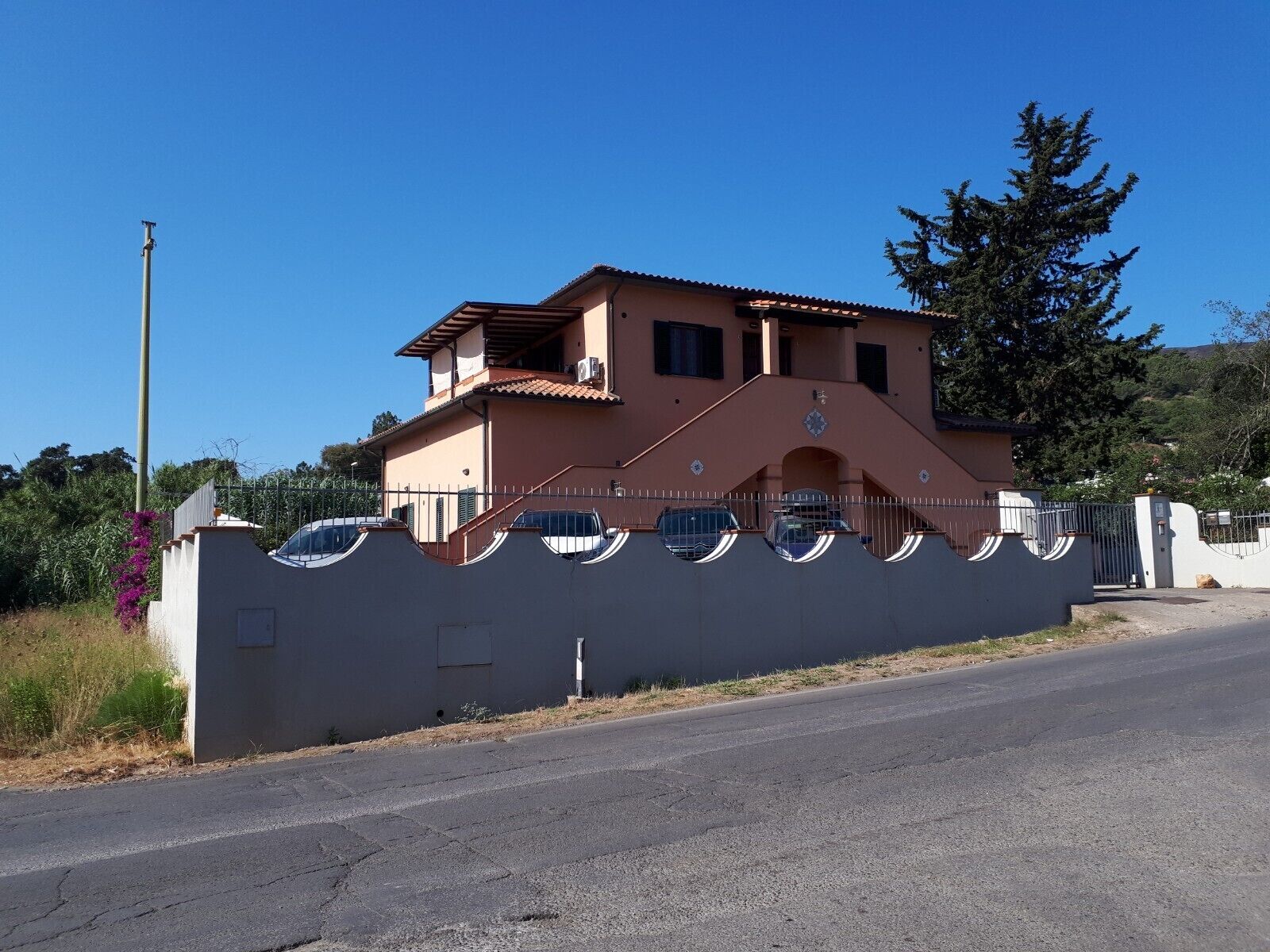 A two-story building with a flat roof, a balcony on the upper floor, and a gated entrance.