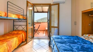 Une chambre avec des lits superposés, un lit simple, une porte-fenêtre coulissante donnant sur un balcon et un ventilateur de plafond.