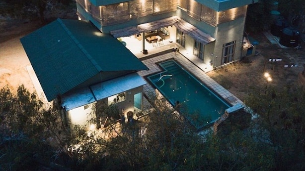 Una casa moderna de dos pisos con piscina, rodeada de árboles y un cielo despejado.