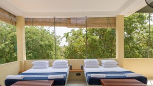 Una habitación con dos camas, cada una con almohadas blancas y ropa de cama azul, una mesita de madera y vistas a árboles verdes a través de amplias ventanas.