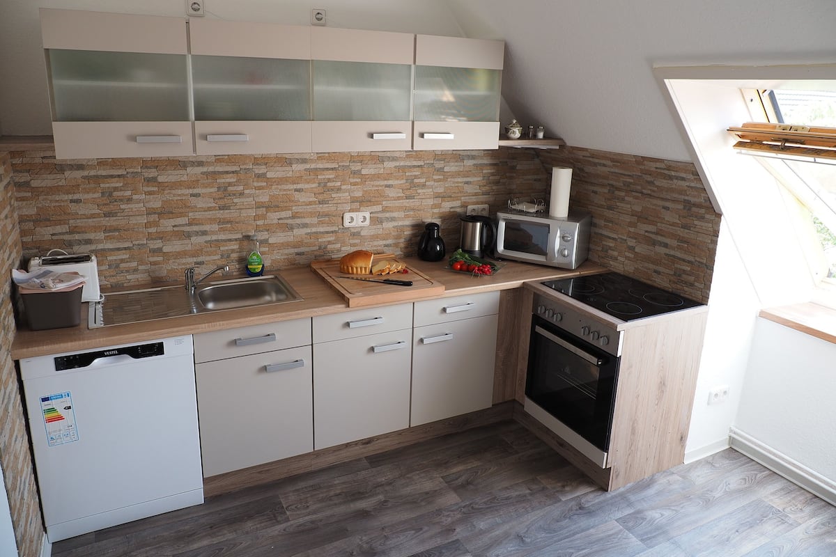 Cocina compacta equipada con lavavajillas, microondas, estufa y protector de salpicaduras de piedra.