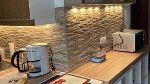 A modern kitchen with a stone backsplash, a built-in oven, a coffee maker, and a microwave on the countertop. - Ferienhof Meyer (Nahrendorf)