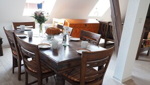 A dining table with six wooden chairs, a vase with flowers, and a cake on a glass stand. - Ferienhof Meyer (Nahrendorf)