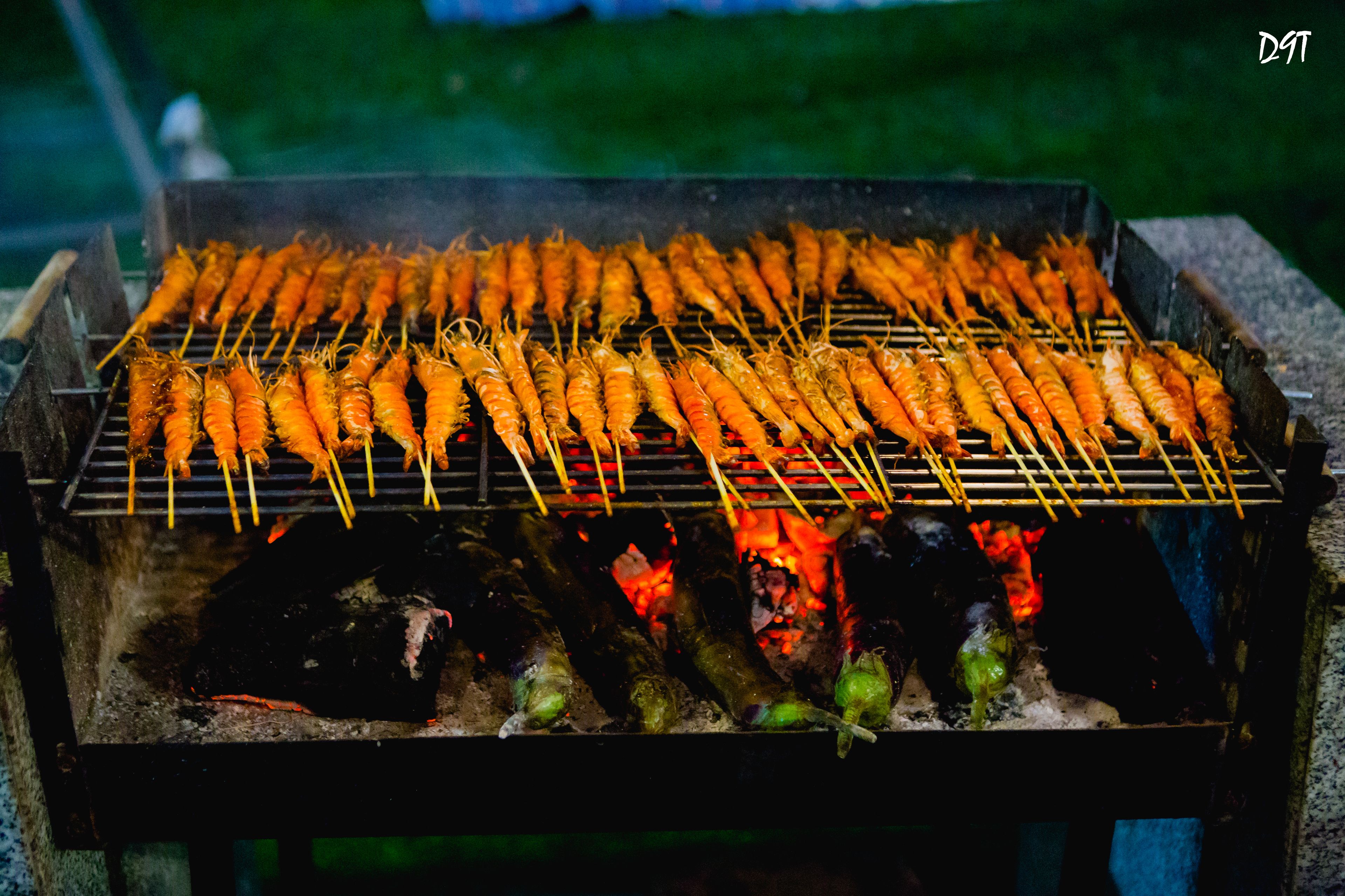 A grill with multiple skewers of food, likely seafood, being cooked over an open flame.