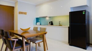 A modern kitchen with white cabinets, a black refrigerator, and a wooden dining table with chairs. - Kim Property Vinhomes Central Park (Ho Chi Minh City)