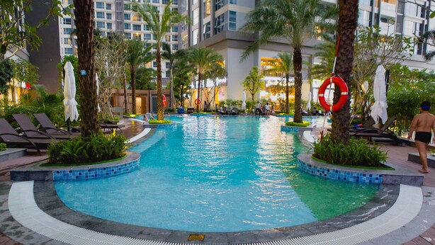 A swimming pool with lounge chairs and palm trees, surrounded by a hotel building. - Kim Property Vinhomes Central Park (Ho Chi Minh City)