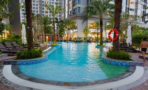 A swimming pool with lounge chairs and palm trees, surrounded by a hotel building. - Kim Property Vinhomes Central Park (Ho Chi Minh City)