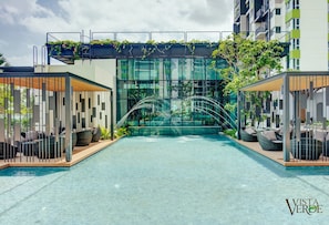 A modern hotel with a rooftop garden, a swimming pool, and outdoor seating areas.
