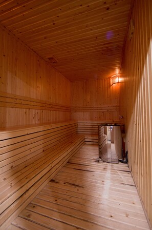 A sauna with wooden walls and benches, a bench in the center, and a small heater on the right.