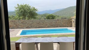 Blick durch eine offene Tür auf einen Poolbereich mit einer Steinmauer und einem Tisch mit Stühlen.