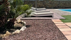 Ein moderner Außenbereich mit Sitzgelegenheit, einer Steinwand im Hintergrund, einem Pool und blauem Himmel.