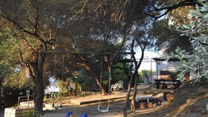 A playground with swings, a slide, and benches under trees. - Villa Anneta (Corfu)