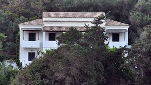 A two-story building with a tiled roof, surrounded by dense forest. - Villa Anneta (Corfu)