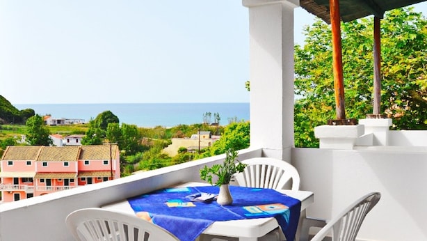 A balcony with a table and chairs, overlooking a coastal view with buildings in the background. - Villa Anneta (Corfu)