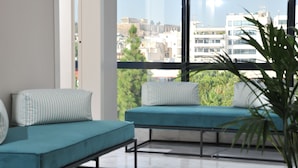 Una habitación moderna con dos sofás turquesa, un ventanal con vistas a la ciudad y una planta en maceta.